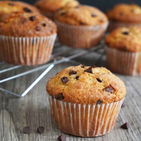 Chocolate Chip Muffin on gray wood board with more muffins on cooling rack in background.