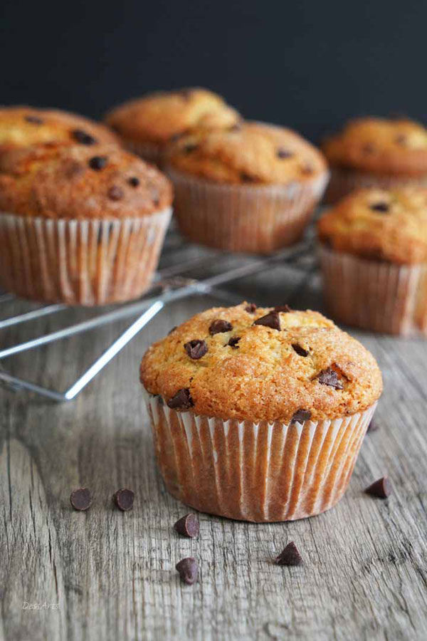 Chocolate Chip Muffin on gray wood board with more muffins on cooling rack in background.