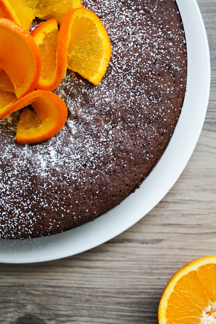 Top view of a quarter of the orange and chocolate flourless cake covered in powdered sugar and orange slice garnish.