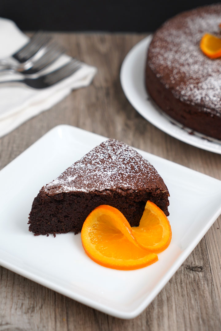 Slice of orange chocolate flourless cake on a white plate with an orange slice garnish.