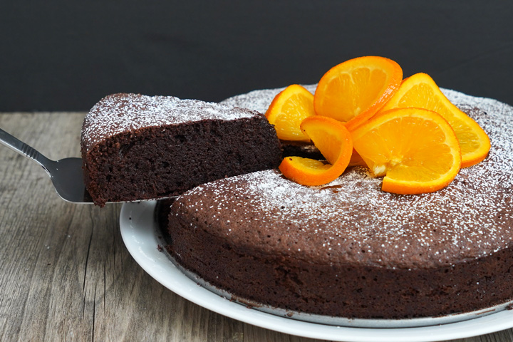 Slice of orange chocolate flourless cake being removed from the cake with a cake server.