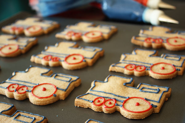 Train shaped sugar cookies outlined with red and blue royal icing on a cookie sheet.