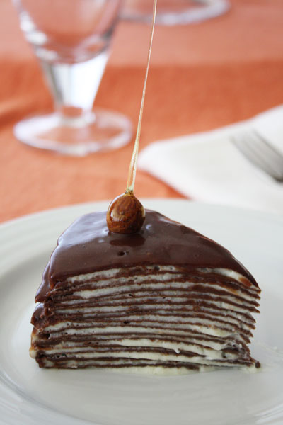 slice of chocolate hazelnut crepe cake with candied hazelnut garnish on top.