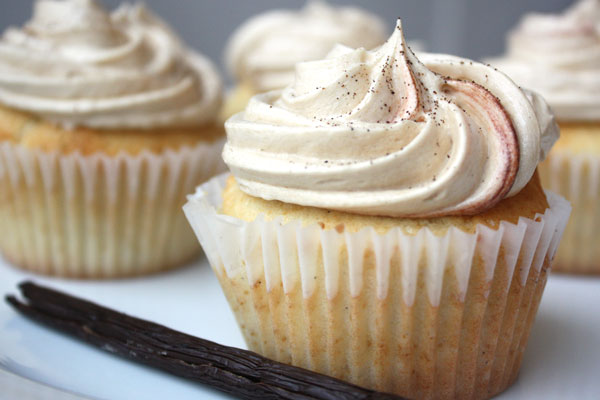 Vanilla bean cupcake with more cupcakes in the background and vanilla bean in the foreground.