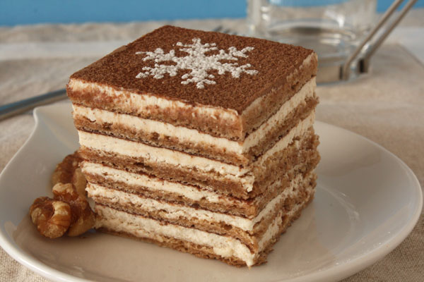 Square piece of cinnamon walnut cake on a white plate with walnuts on the side.