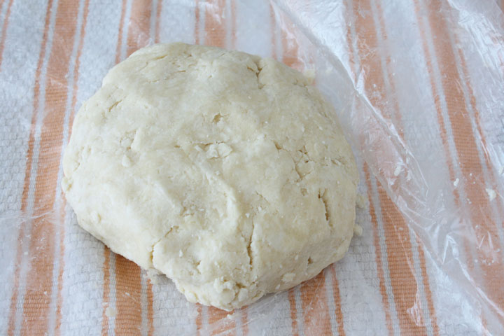 Pie dough ball in being wrapped in plastic.