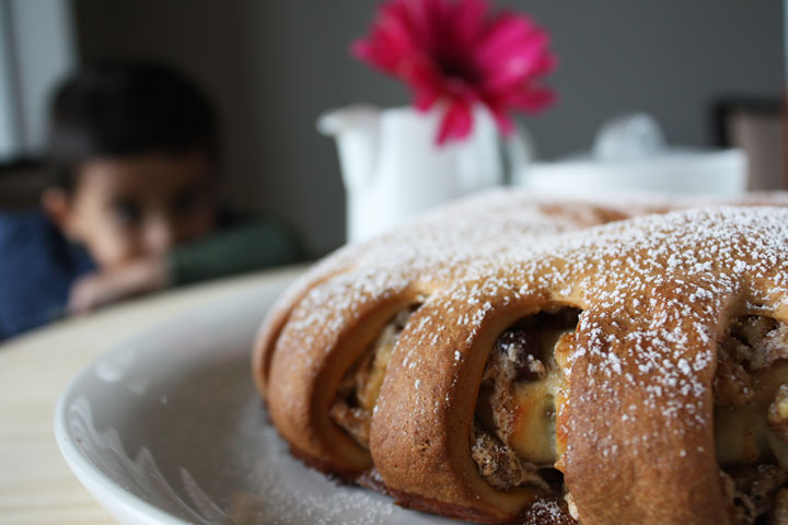 Close up view of meringue Coffee Cake is stuffed with chocolate, cinnamon and walnuts on a white plate with child viewing in the background.