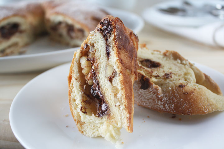 Two slices of meringue Coffee Cake is stuffed with chocolate, cinnamon and walnuts on a white plate with remaining cake in the background.