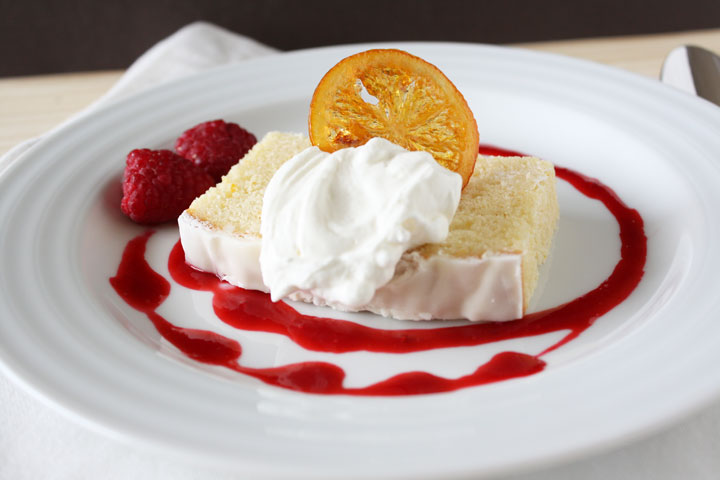  Postre plateado de pastel de limón con coulis de frambuesa, crema batida y una rodaja de limón confitada.