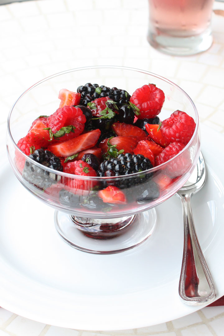 Top view of summer berry salad cocktail without ice cream in a clear glass footed bowl with spoon on the side. 