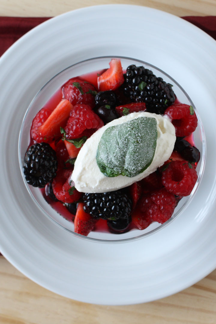  Top view of summer berry salad cocktail with ice cream and frosted basil leaf. 