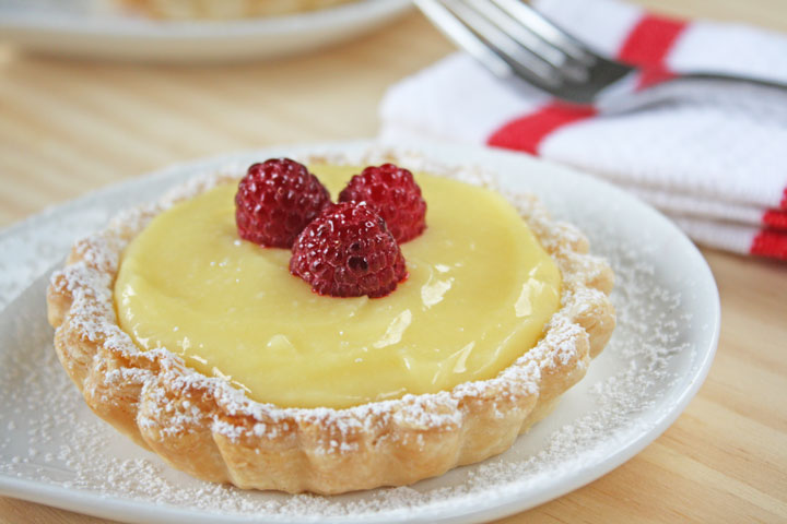 Lemon Tart closeup on a white plate with fork and napkin in the background.