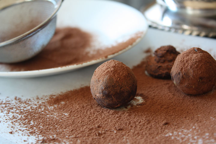 Cardamom chocolate truffles being rolled in cocoa powder on a sheet of parchment.