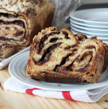 Sliced of chocolate babka on a white plate with chocolate babka loaf in the background.