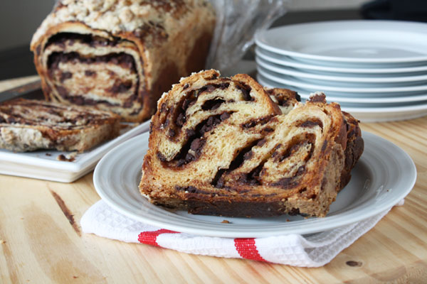 Sliced of chocolate babka on a white plate with chocolate babka loaf in the background.