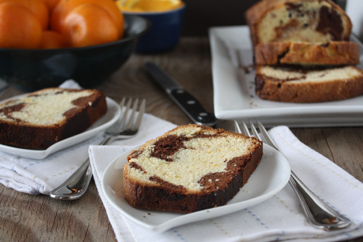 Marble orange point cake slices on white plates with oranges and loaf in background