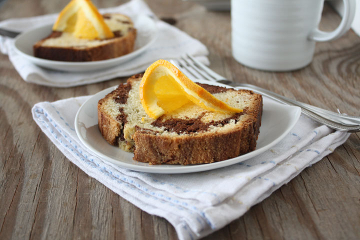 Two slices of marble orange poundcake on plates with orange slice garnish