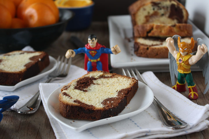 Orange Marble pound cake slice shown with superman and hackman toys on the table.