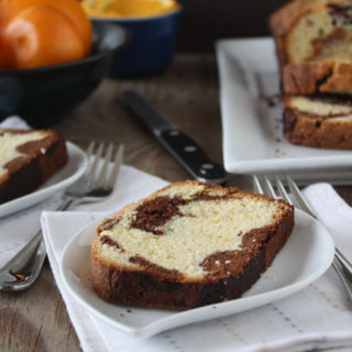 Marble orange point cake slices on white plates with oranges and loaf in background