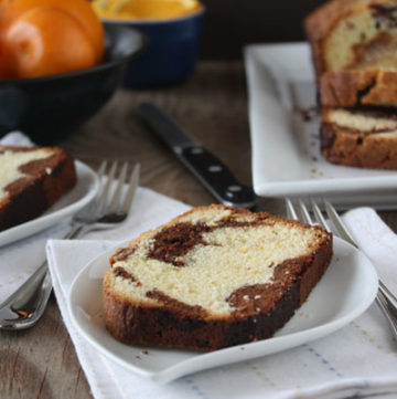 Marble orange point cake slices on white plates with oranges and loaf in background