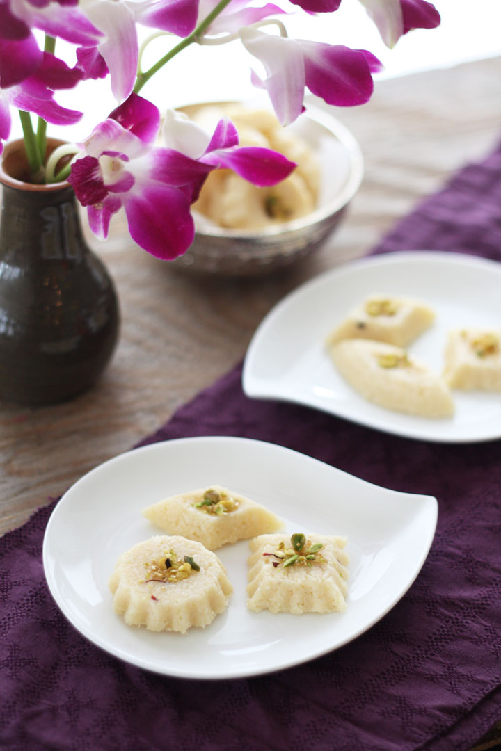 Two plates of coconut burfis on a purple runner next to orchids in a vase.