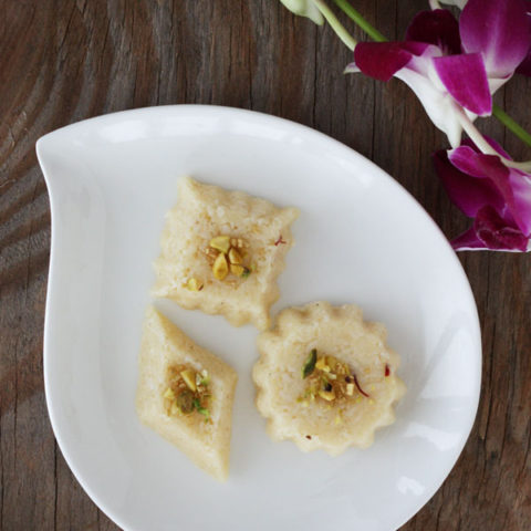 Three differently shaped coconut burfi in a white plate. Birds eye view.