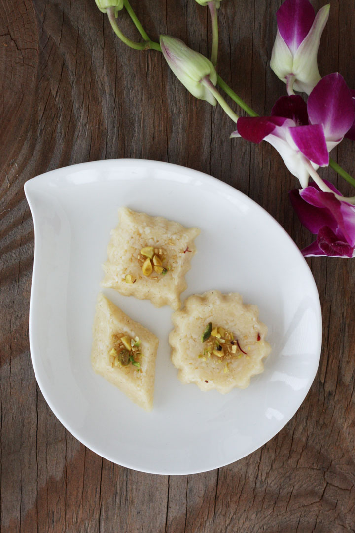 Three differently shaped coconut burfi in a white plate. Birds eye view.