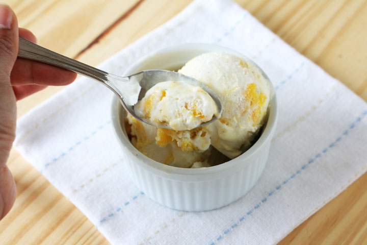 Spoon of ice cream being taken from mango swirl ice cream in a white bowl.