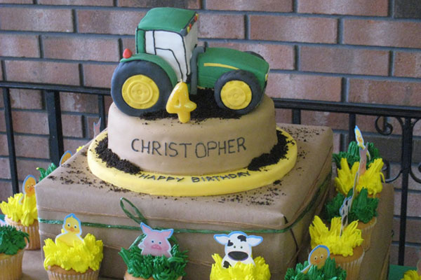 John Deere Tractor Cake on stand with surrounding matching farm cupcakes.