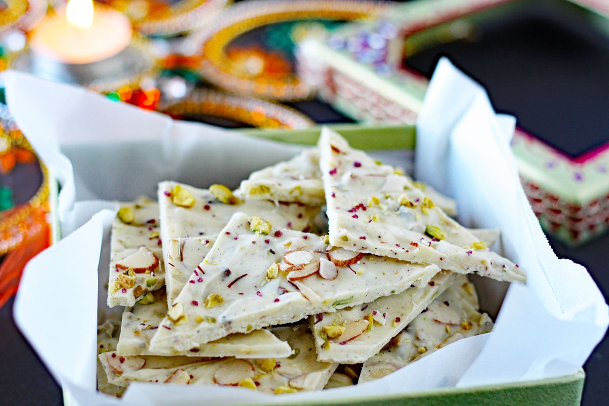 Pieces of white chocolate bark with pistachios, almonds, and cardamom in a box ready for Diwali gifting. 