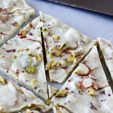 Pistachio white chocolate bark with cardamom and rose cut up on parchment paper.