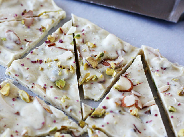 Pistachio white chocolate bark with cardamom and rose cut up on parchment paper.