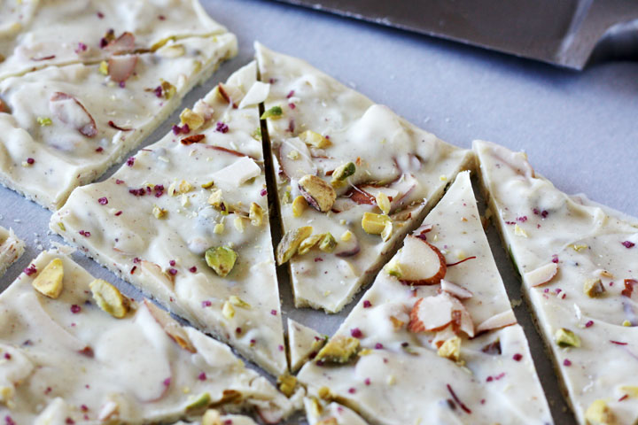 Pistachio white chocolate bark with cardamom and rose cut up on parchment paper.