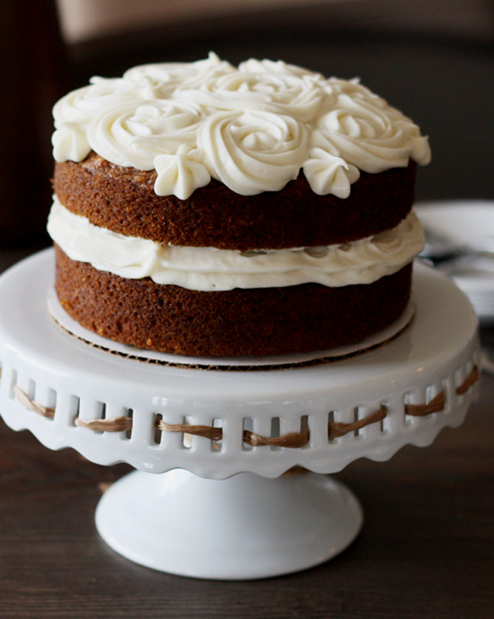 Simple 6 inch carrot cake with cream cheese frosting on a white pedestal stand.