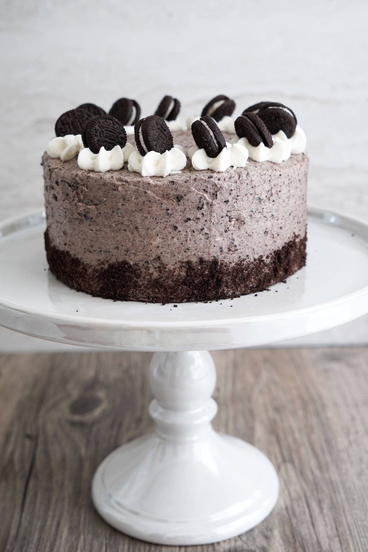 Mini cookies and cream chocolate cake with mini Oreos around the top edge on a white cake stand