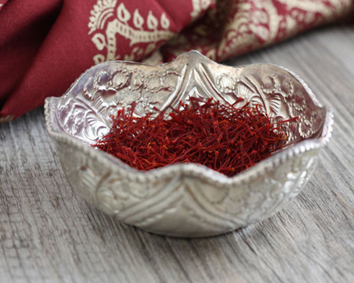 Decorated silver bowl full of saffron strands with red napkin in the background.