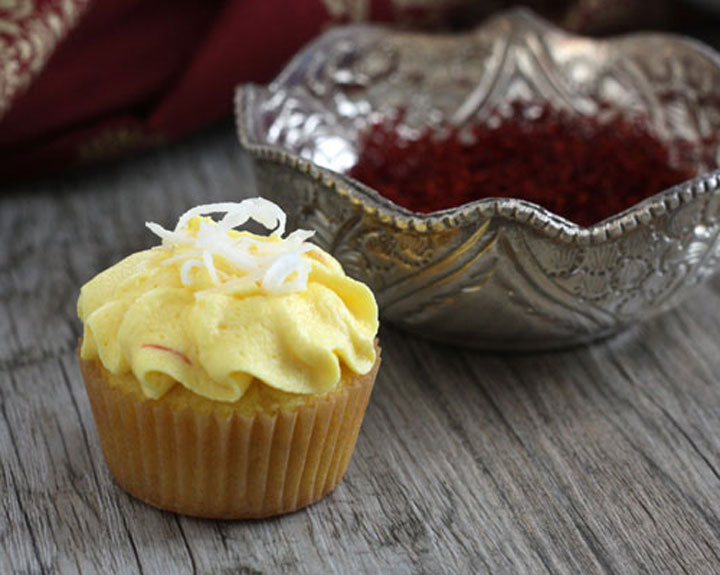 Saffron cupcake with coconut garnish in front of silver bowl full of saffron threads.