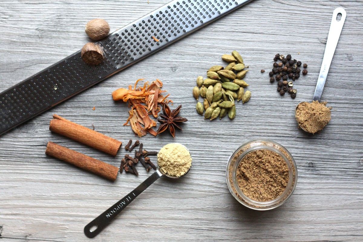 Overhead shot of chai spice mix in jar, whole spices and nutmeg grater.