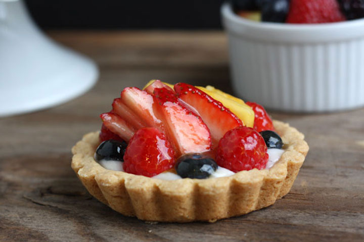 Mini tarta owocowa z truskawkami, borówkami i ananasem pokryta błyszczącą glazurą.