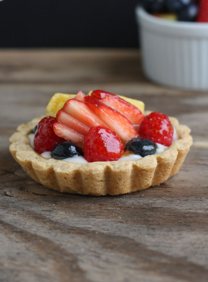 Close up of mini fruit tart with strawberries, blueberries and pineapple topped with a shiny glaze.