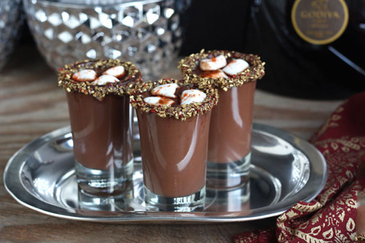 Three Mexican hot chocolate shots with marshmallows and decorated rims in a silver tray.