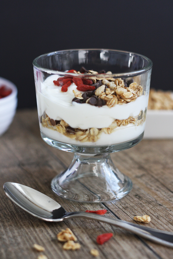 Yogurt parfait with vanilla yogurt, granola, goji berries and chocolate chips in a stemmed dessert glass. 