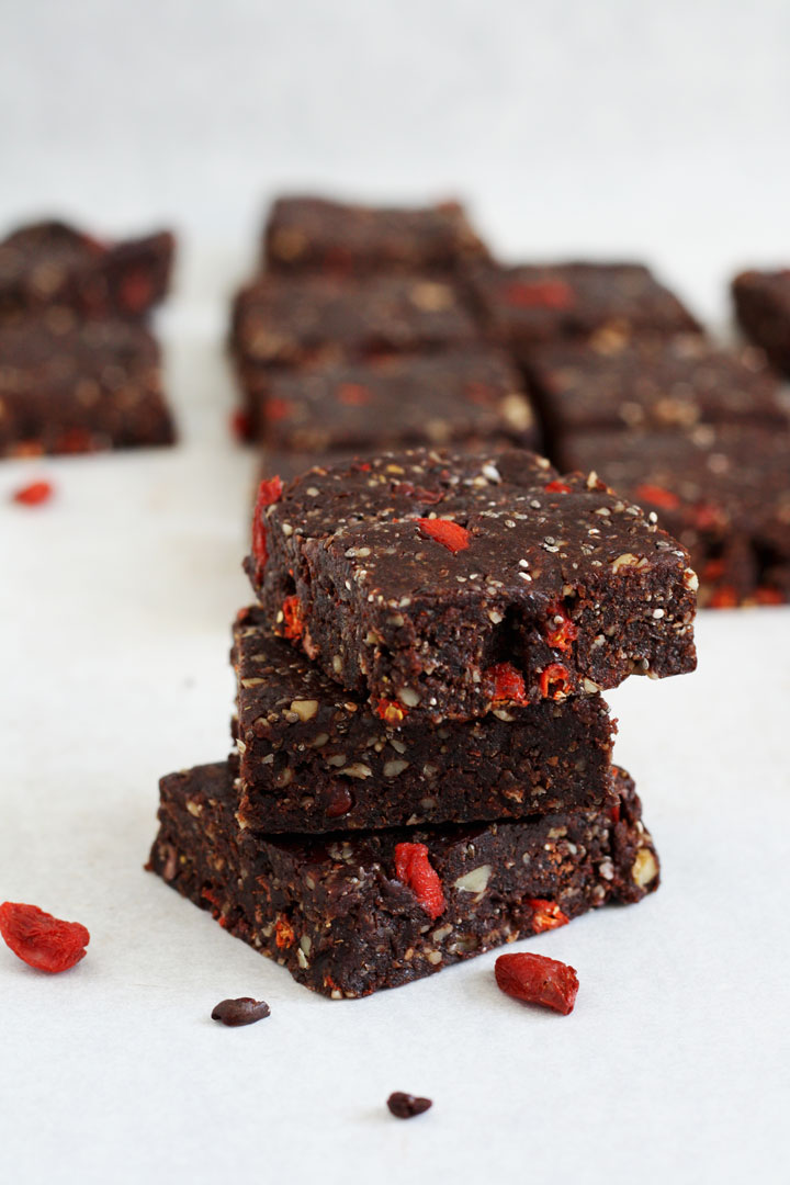 Stack of three no bake healthy brownnies with goji berries and cacao nibs on the side.