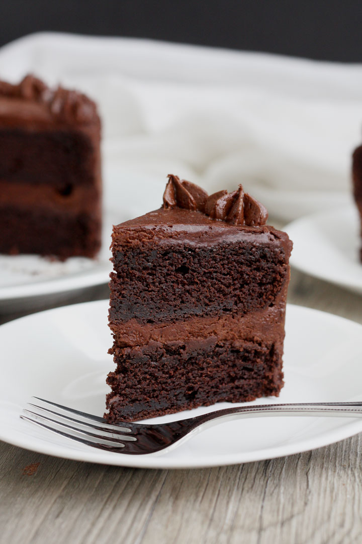 Slice of chocolate cake with fudge frosting in white plate.