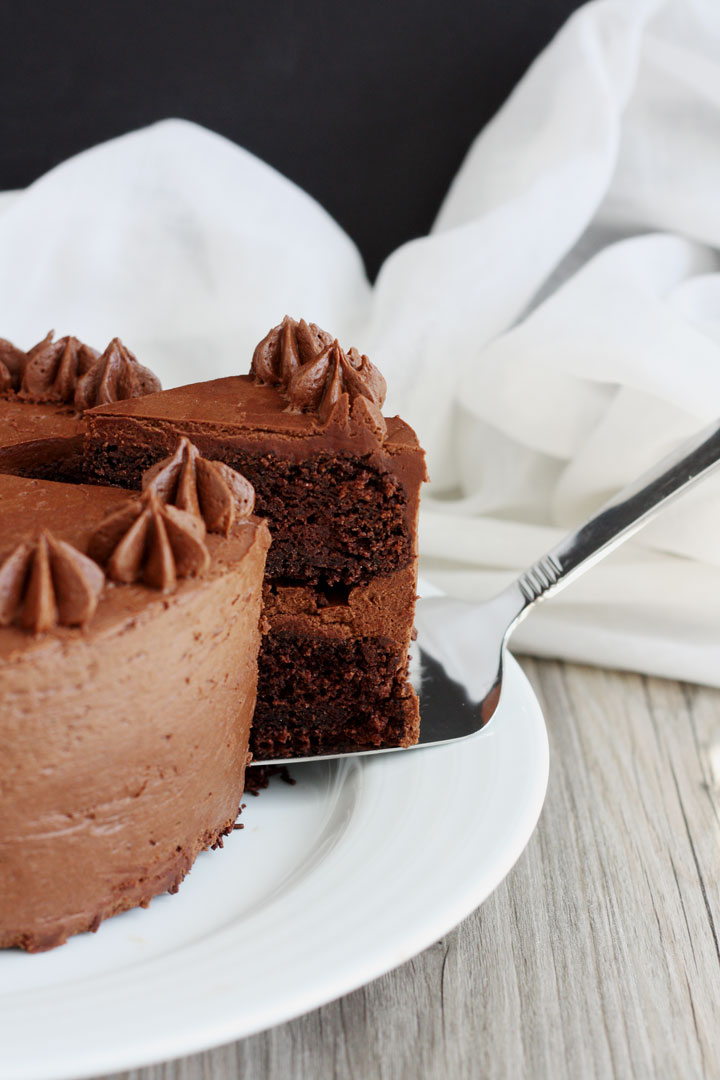 Slice of chocolate cake topped with fudge frosting being removed form the whole cake.