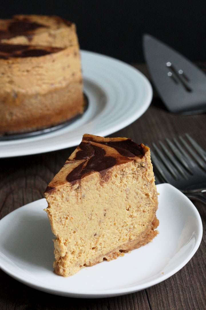 Slice of pumpkin cheesecake with chocolate swirl top in white plate.