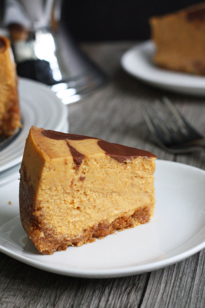 Slice of pumpkin cheesecake with chocolate swirl top in white plate.