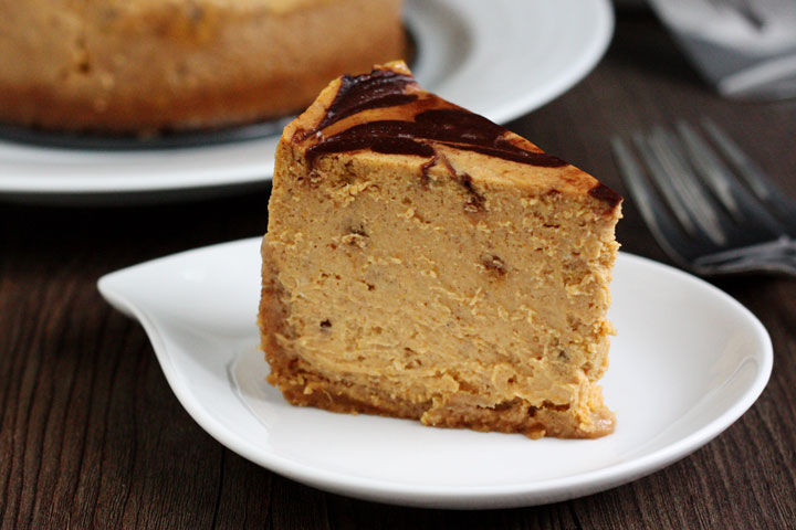 Slice of pumpkin cheesecake with chocolate swirl top in white plate.