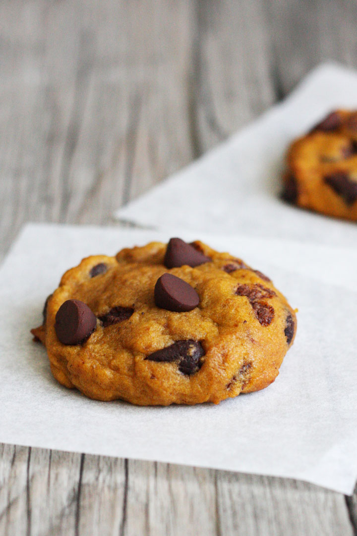 Single pumpkin chocolate chip cookie on parchment paper square.