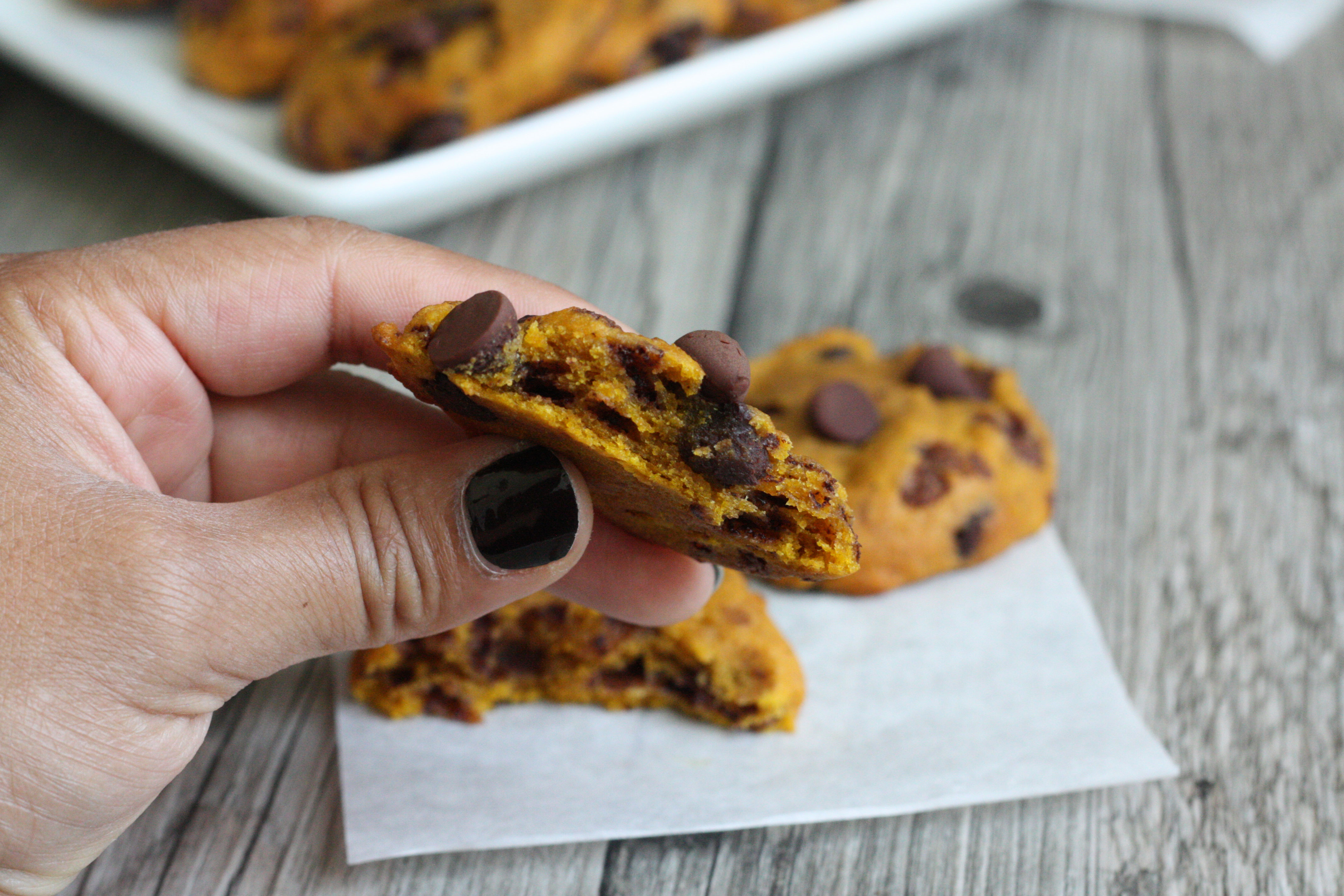 Hand holdind up a bitten pumpkin chocolate chip cookie showing the center.